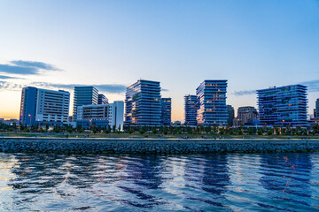 Fototapeta premium Vue panoramique des buildings modernes du quartier de Zeytinburnu à Istanbul, photographiés depuis un bateau sur la mer de Marmara. Le coucher du soleil illumine les façades vitrées des immeubles, tan