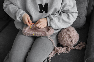 Obraz premium Girl knits slippers on a gray sofa, hobby concept