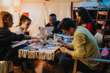 A group of friends gathers around a table, engaging in creative painting activities, fostering...