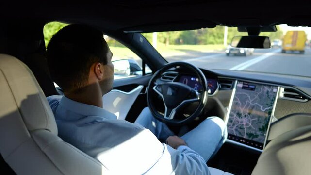 Male businessperson experience to ride an autonomous self driving electric car at urban road. Confident businessman resting during riding on electrical auto with autopilot at city. Slow motion