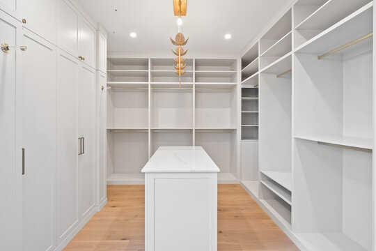 A large, empty walk in closet with white cabinets and a white counter