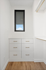 A small white closet with a window and a white dresser