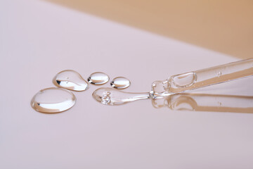A pipette with a few drops of serum on a beige background.