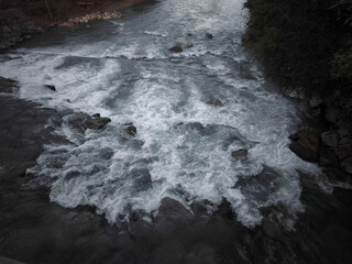 Raging river cutting between rocky mountain slopes, rushing past verdant landscape, displaying powerful natural dynamics