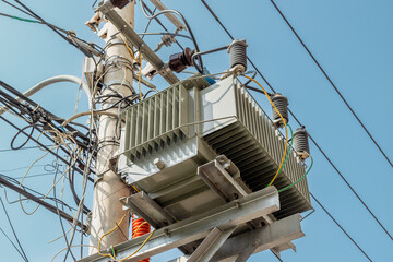 Electrical transformer on utility pole with cables and insulators under blue sky