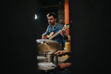 Fototapeta premium Band rehearsal featuring a focused musician playing a bass guitar in a studio, creating a lively and artistic atmosphere. The dark ambiance and warm light enhance the setting.