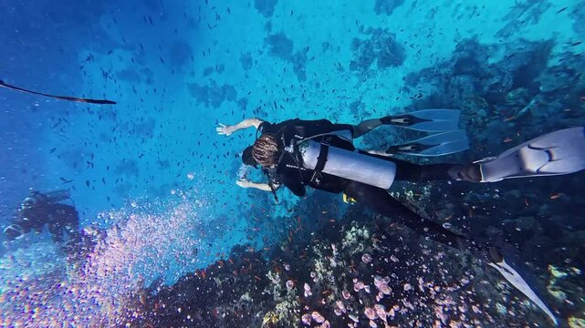 Group of scuba divers swimming between corals at coral reef. Diving instructor and group students in underwater exercise. Instructor teaches students. Underwater scuba diving education and training.