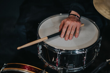 A detailed perspective showing a hand holding a drumstick, placed atop a beautifully polished snare drum. The background enhances the focus on the musician's dedication to their craft.