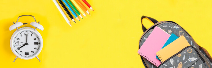 Back to school. School backpack and white alarm clock on a yellow background. Copy space. Top view.