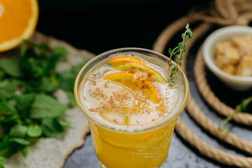 Refreshing citrus cocktail with orange slices, cinnamon and herbs in glass on dark background