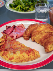 Breakfast pizza slice, croissant, ham, greens and beverages water and juice