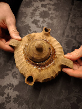 Weathered hands cradling handcrafted wooden teapot on rustic linen, artisan woodworking detail from aosta valley, italy coffee in the grolla