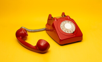 A vibrant red rotary phone with a glossy finish sits against a bold yellow background. The handset...