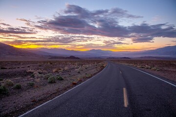 Scenic desert road at sunset with colorful clouds and mountain backdrop