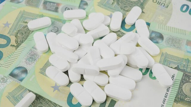 Image of white pills scattered on European banknotes, highlighting healthcare costs and pharmaceutical finance. Represents topics of economic aspects of medicine, affordability, and pharmaceutical ind