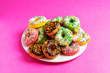 Colorful donuts on a white plate on red, pink background.