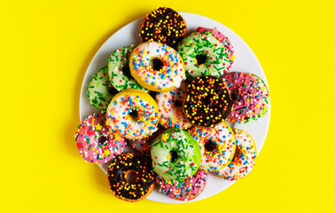 Colorful donuts on a white plate on yellow background
