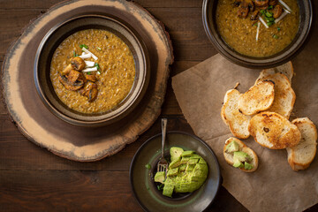 Vegan cream of mushroom soup on wooden table along with toasted bread and avocado