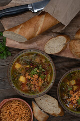 Beet greens and potato soup with bread and crispy onion, wooden background