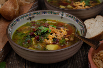 Beet greens and potato soup with bread and crispy onion, wooden background close up