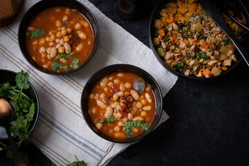 Vegan bean and garbanzo soup along with salad bowl served in black bowls on dark backround