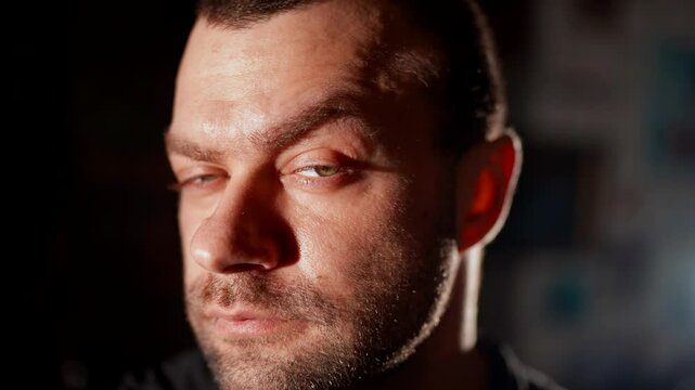 A man looks away with a squint, creating a mysterious and slightly tense image. The light and shadows play on his face, adding drama.