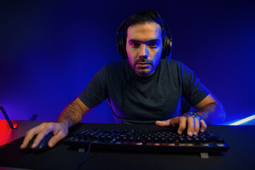 Smart gaming streamer concentrating gaming players trying to pass the level at mission completed, using headset and mic for communicate others on streaming live at neon lighting studio room. Surmise.
