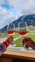 Two glasses of Rosé are raised in a toast, with a scenic view of Matrei in Osttirol, Austria, in...