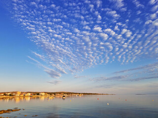 Scenic coastal town with rippled cloud formations over calm sea at sunset