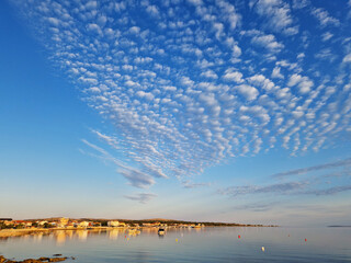 Scenic coastal town with rippled cloud formations over calm sea at sunset