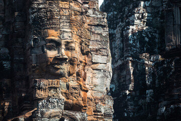 Weathered statue of serene and smiling stone face on Bayon temple, in Angkor Thom. Siem Reap,...