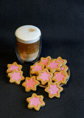 Glass of cappuccino with cookies on a dark background. Cup of coffee and Christmas cookies (cinnamon stars) on a dark background. Delicious latte macchiato and cookies. Close up.