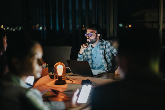 Focused professionals work late in a dimly lit office, collaborating intensely on a project. The ambiance is intimate and productive, highlighting teamwork and dedication to their business objectives.