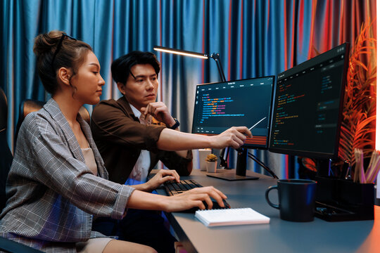 IT developers discussing with point to intelligent website development coder system running data online two screens information technology at neon light room at modern office. Infobahn.