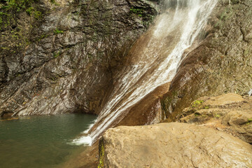 A high waterfall in a green forest with rocks