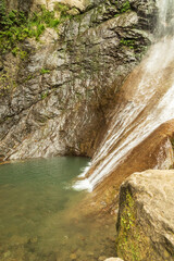 A high waterfall in a green forest with rocks