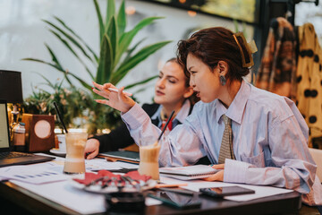 Two business people working together, analyzing data and strategizing, while spending time in a relaxed, modern environment. They are seeking innovative ideas over a table with notebooks and a laptop.