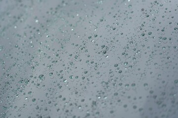 A close-up shot of raindrops scattered across a glass surface, forming an abstract and organic pattern.