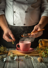 The cook brews healthy tea from medicinal dry herbs. The hand holds a spoon with dry rose hips that need to be added to a pink cup. The concept of traditional medicine and prevention of viral diseases