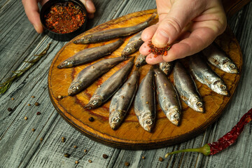 Freshly caught fish lay on a wooden board, as a hand sprinkles vibrant spices over them. The rustic...