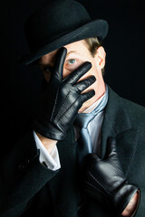 Gentleman in Dark Formal Suit and Bowler Hat and Leather Gloves Held in Front of Face. Vintage Style and Retro Fashion.