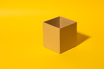 Fototapeta premium A simple open cardboard box sits against a vibrant yellow background, creating a striking minimalist composition. The clean lines and neutral tones emphasize the concept of packaging, shipping