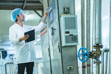 Worker examining an industrial tank and recording data on a clipboard, emphasizing the importance of safety, quality assurance, and technological advancement in industrial environments.