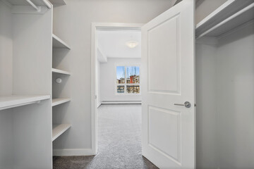 White closet with a door open and a window in the background