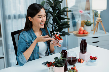 Smiling young beautiful Asian reviewing tasty mixed strawberry and cherry juice detox drinks,...