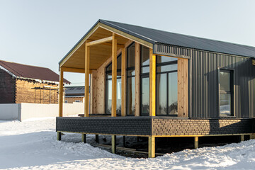 Construction of a frame house. One-storey dark grey modular house. Stilt house with terrace. Wooden...