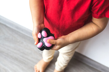 A child in a red T-shirt holds a paw-shaped squishy toy taba paw in their hands, pressing it for stress relief and sensory play