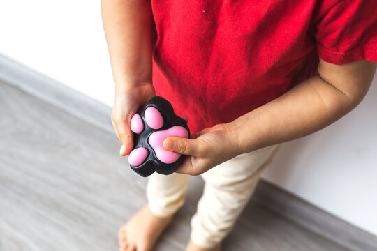 A child in a red T-shirt holds a paw-shaped squishy toy taba paw in their hands, pressing it for stress relief and sensory play