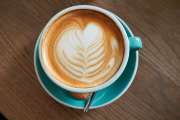 Cappuccino in a beautiful turquoise porcelain cup on a wooden brown table. A beautiful heart made of cappuccino foam.