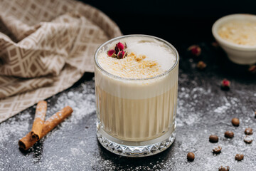 Creamy latte with coconut flakes and dried rose garnish, served in a glass with a velvety frothy top